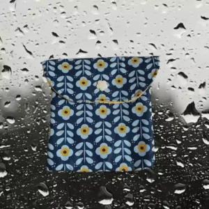 Pochette carrée fermée par une pression en forme de fleur jaune. En tissu enduit motif fleur avec tige sur fond bleu.