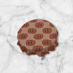 Charlotte alimentaire taille bol en tissu enduit au motif pomme avec un visage couleur saumon sur fond saumon clair